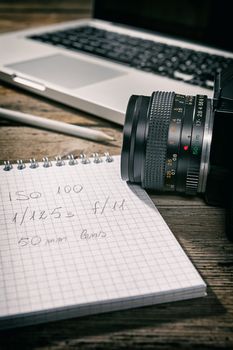 Closeup of a written notebook and a camera with a laptop on background