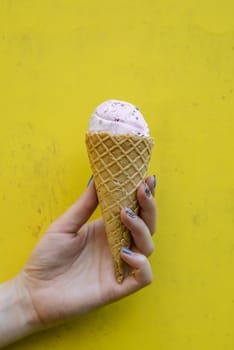 ice cream in waffle cup in female hand on yellow background