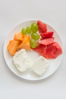 sliced watermelon, cantaloupe, cottage cheese and green grapes in a white plate on a white background