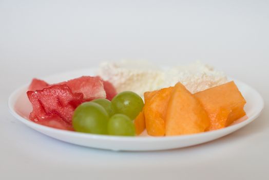 sliced watermelon, cantaloupe, cottage cheese and green grapes in a white plate on a white background