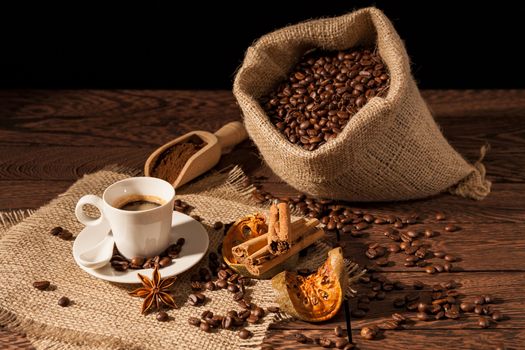 Coffee cup with cinnamon, star anise, dried orange fruit and coffee sack over a wooden background