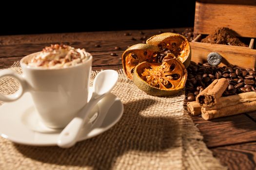 Close-up of coffee cup, dried orange fruit and cinnamon sticks over a wooden background