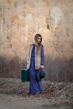 pretty young woman with a leather suitcase on a dirtroad in the mountains, vintage style