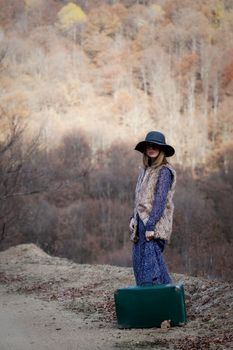 pretty young woman with a leather suitcase on a dirtroad in the mountains, vintage style