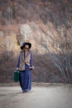 pretty young woman with a leather suitcase on a dirtroad in the mountains, vintage style
