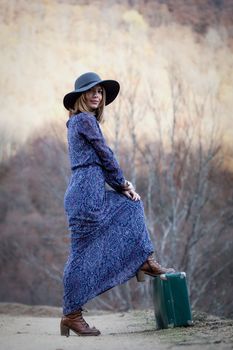 pretty young woman with a leather suitcase on a dirtroad in the mountains, vintage style