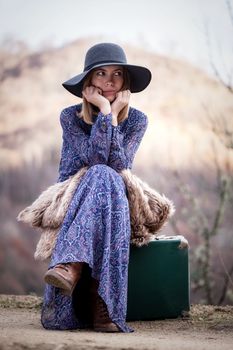 pretty young woman with a leather suitcase on a dirtroad in the mountains, vintage style