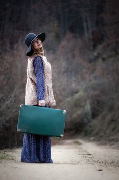 pretty young woman with a leather suitcase on a dirtroad in the mountains, vintage style