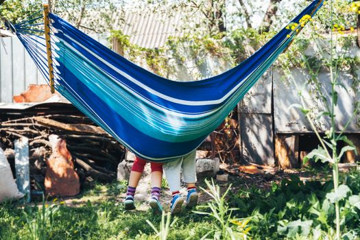 Children's feet in blue hammock on a background of nature greenery.