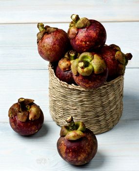 Arrangement of Fresh Ripe Mangosteen in Wicker Box closeup on Light Blue Wooden background