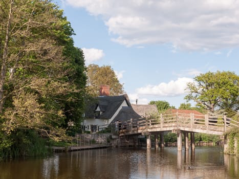 the bridge at flatford mill leading to a cottage in the heartland of constable country essex and suffolk near Dedham with people on the bridge viewing on a sunny relaxing afternoon in peace
