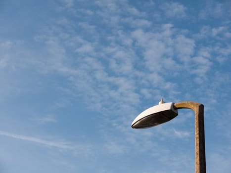 the top of a street light outside turned off during day with a blue and white sky broken not working and turned off spring day