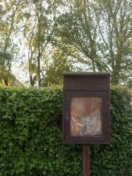 close up of a brown old and unused wooden notice board outside near a park sign without notices