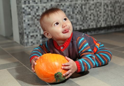 little boy of eight months holding not big orange pumpkin