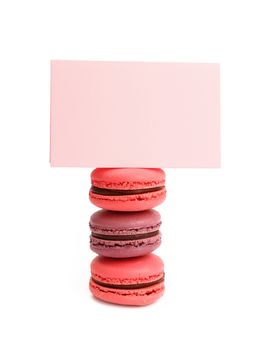 Stack of colorful traditional French macaroon pastry cookies (macarons, macaroni) with pink paper sign isolated on white background, close up, low angle view