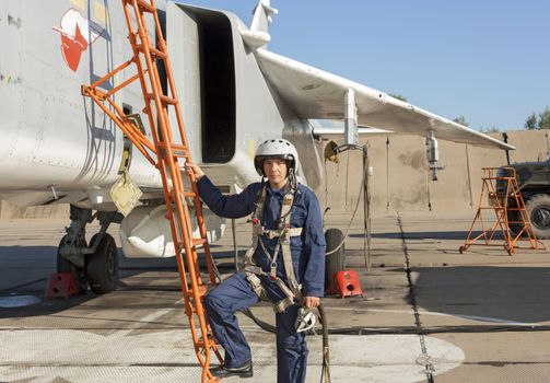 Military pilot in helmet stands near jet plane.