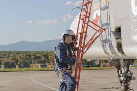 Military pilot in helmet stands near jet plane.