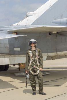 Military pilot in helmet stands near jet plane.