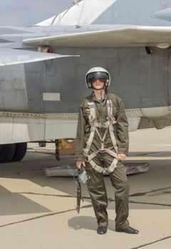 Military pilot in helmet stands near jet plane.