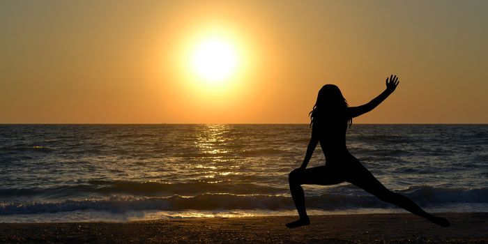 Woman silhouette in a yoga pose on the beach at sunrise