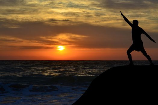 Man black silhouette in a yoga pose on the shore at sunrise