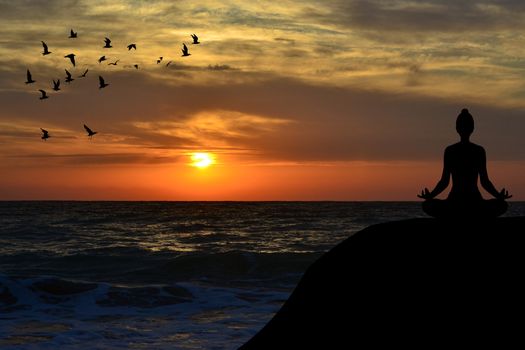 Woman silhouette meditating in a yoga pose on the beach at sunrise