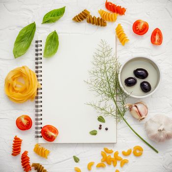 Italian foods concept and menu design . Various pasta elbow macaroni ,fusilli ,fettucini with ingredients sweet basil, sage ,black olive ,himalayan salt ,pepper and garlic setup on white notebook .