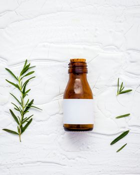 Fresh branch of rosemary  with bottle essential oil setup on white wooden table. Nature aromatherapy spa oil with flat lay on white table.