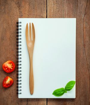 Foods background and Food menu design sweet basil and cherry tomatoes sliced  setup with white notebook on dark shabby wooden table. Foods stylist vegetables and utensils on wooden background with flat lay.