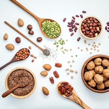Bowls and spoons of various legumes and different kinds of nuts walnuts kernels ,hazelnuts, almond kernels,brown pinto ,soy beans ,flax seeds ,chia ,red kidney beans and pecan set up on white wooden table.