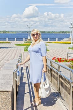 Blond woman in blue dress standing on embankment