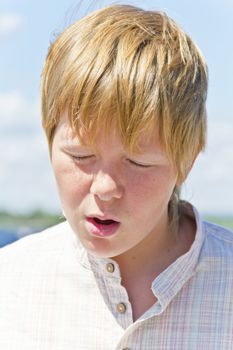 Portrait of squint blond boy in a white shirt near river