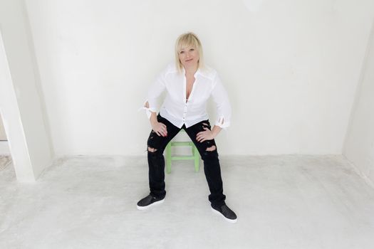 Blond woman in white and black jeans sitting on green stool inside empty room