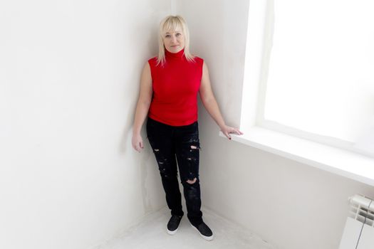 Blond woman in red and black jeans stand inside empty room