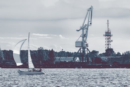 Sailboat moving past the cargo crane in evening, Latvia