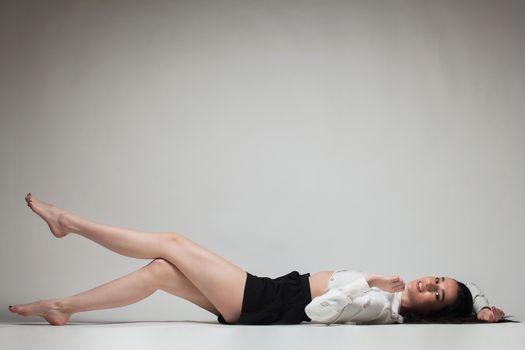 full body shot of beautiful black haired lady lying on the ground bare feet