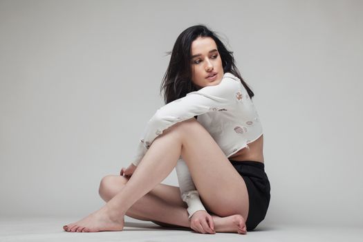 full body shot of beautiful black haired lady sitting on the ground bare feet