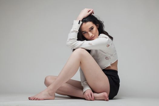 full body shot of beautiful black haired lady sitting on the ground bare feet