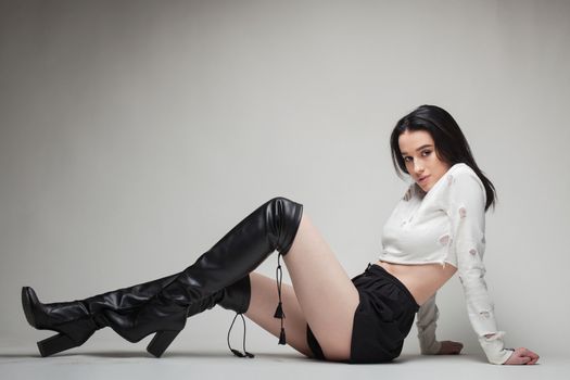 full body shot of beautiful black haired lady wearing high heels boots, sitting on the ground