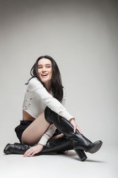 full body shot of beautiful black haired lady wearing high heels boots, sitting on the ground