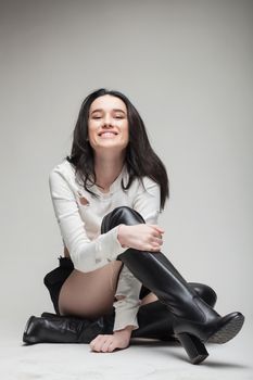 full body shot of beautiful black haired lady wearing high heels boots, sitting on the ground