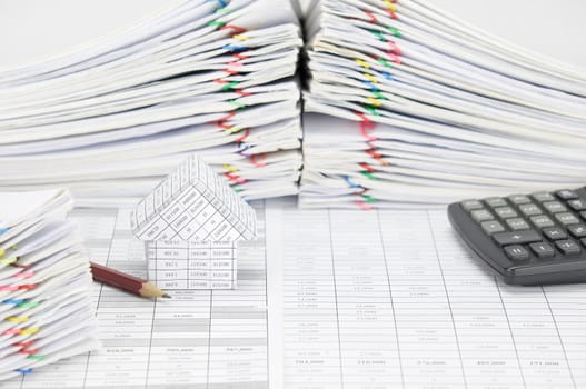 House and pencil on finance account have blur pile overload document of report and receipt with colorful paperclip and calculator as background.