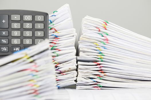 Pile overload document of report and receipt with colorful paperclip and calculator place vertical on finance account have blur pile overload paperwork as foreground.