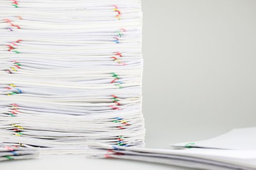 Pile overload paperwork of receipt and report with colorful paperclip on left have blur pile document around on white table.