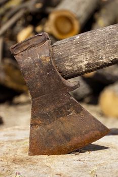 Close up shot of an axe in a stump with firewood in the background.