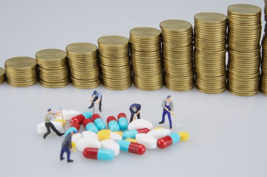 Medicine and blur of pile coins with miniature people on white background.