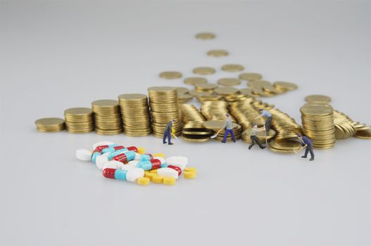 Stack of gold coin with miniature people and medicine on white background.