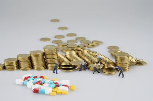 Stack of gold coin with miniature people and medicine on white background.