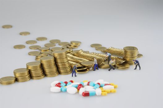 Stack of gold coin with miniature people and medicine on white background.