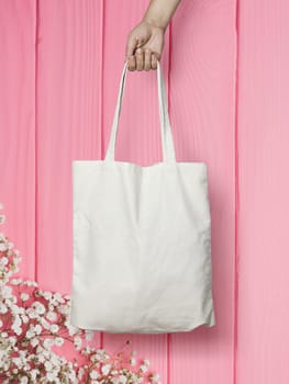 female hand holding a cloth bag on pink wooden background